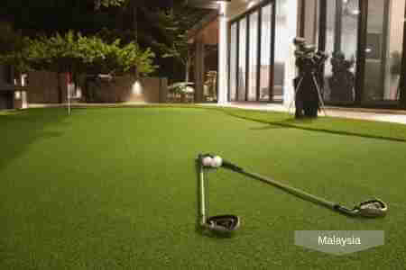 A nighttime golf practice area in Malaysia featuring artificial grass, golf clubs, and balls